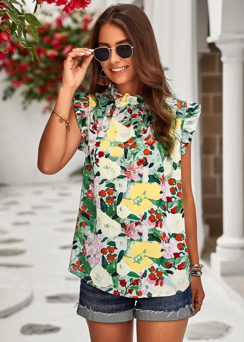 Woman in a colorful floral print top with ruffled sleeves and denim shorts, wearing sunglasses.