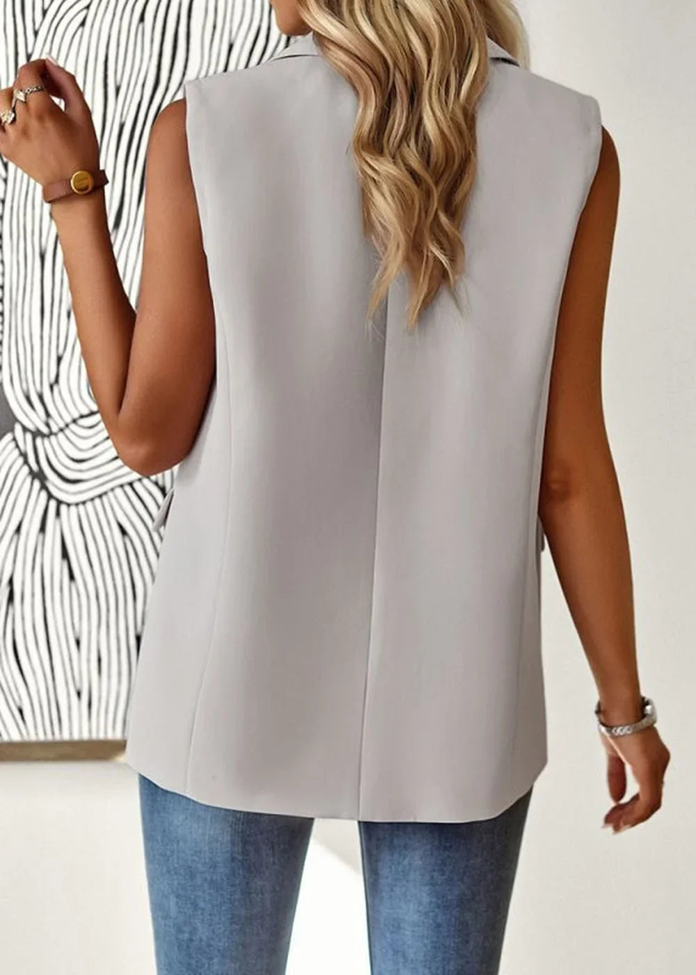 Back view of a light gray sleeveless blazer on a model wearing blue jeans.