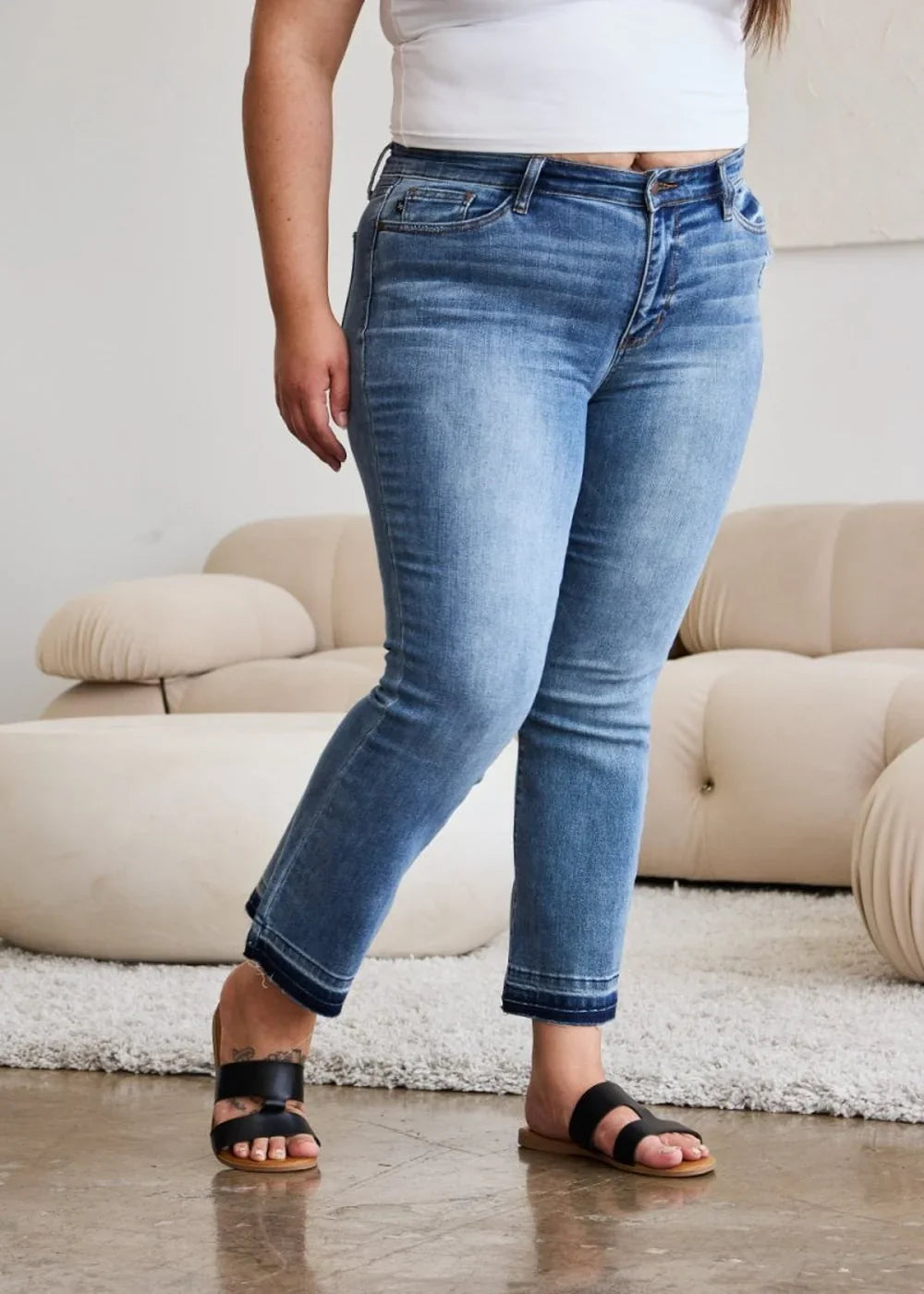 Medium wash distressed denim jeans with frayed hem, worn by a model.