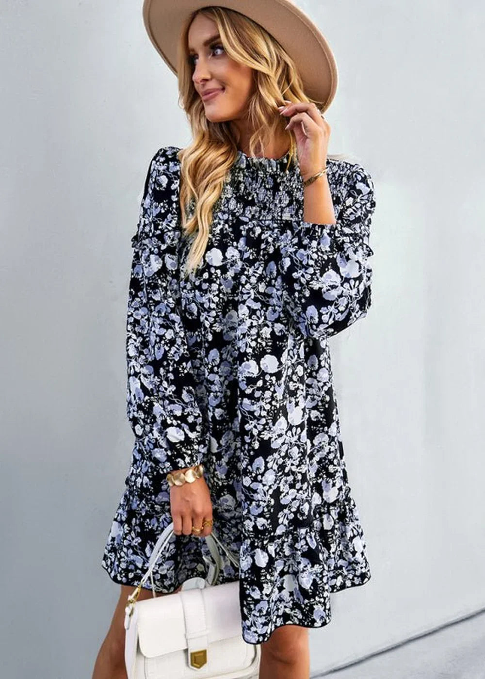 Black floral print dress with smocked bodice, ruffled hem, and white handbag on a woman wearing a tan hat.