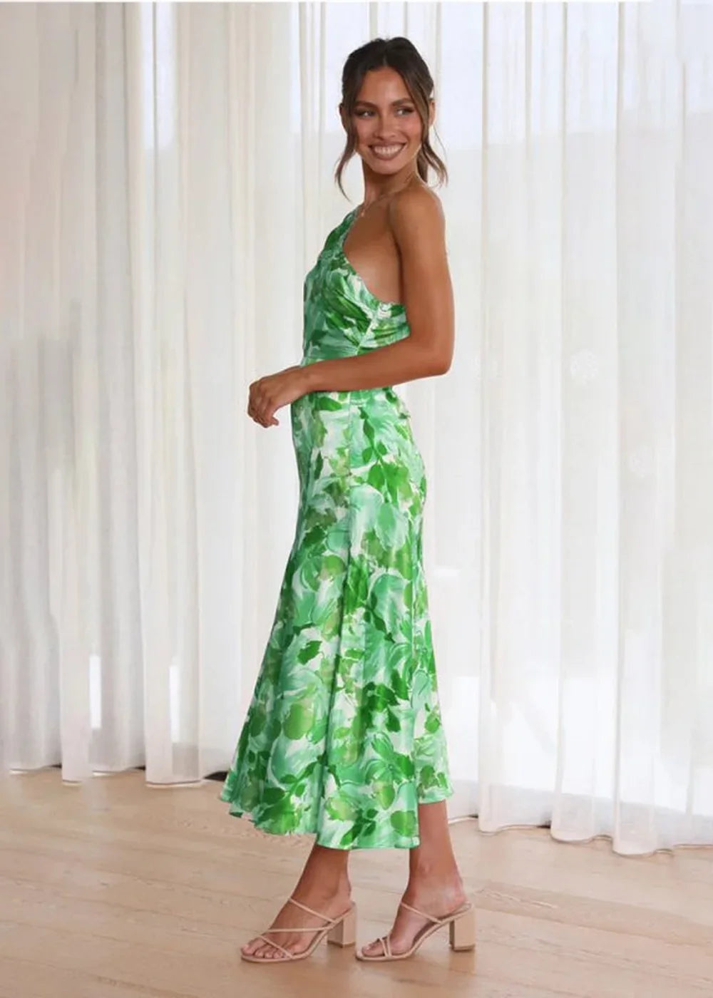 Woman in a flowing green floral print maxi dress with a one-shoulder neckline and nude heels.