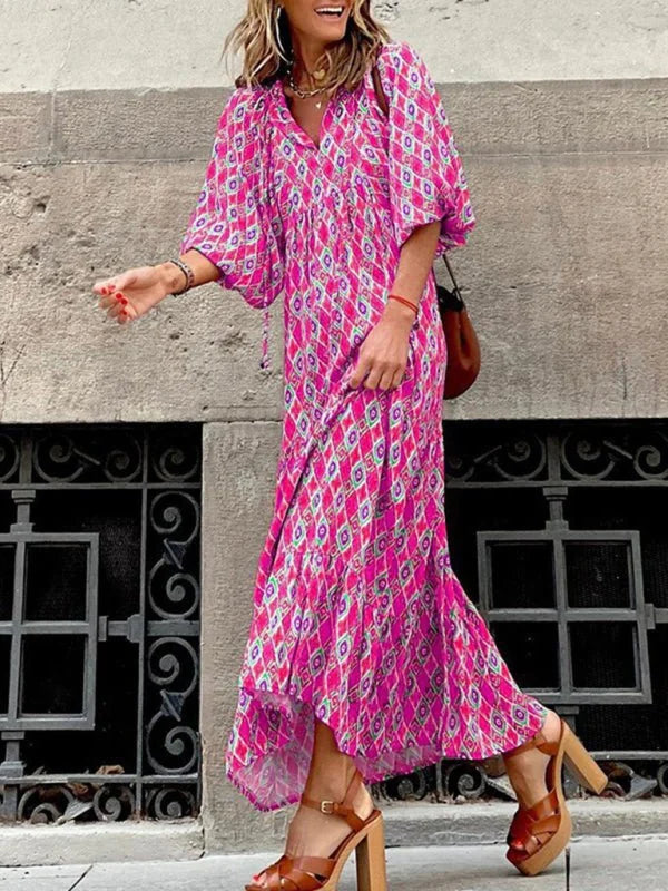 Woman in a flowing pink geometric maxi dress with puffed sleeves and brown platform sandals.