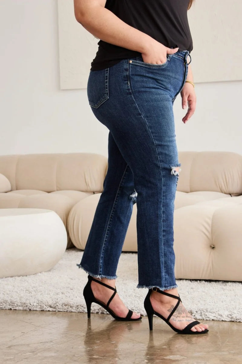 Woman wearing dark wash distressed denim jeans with frayed hems and black strappy heels.