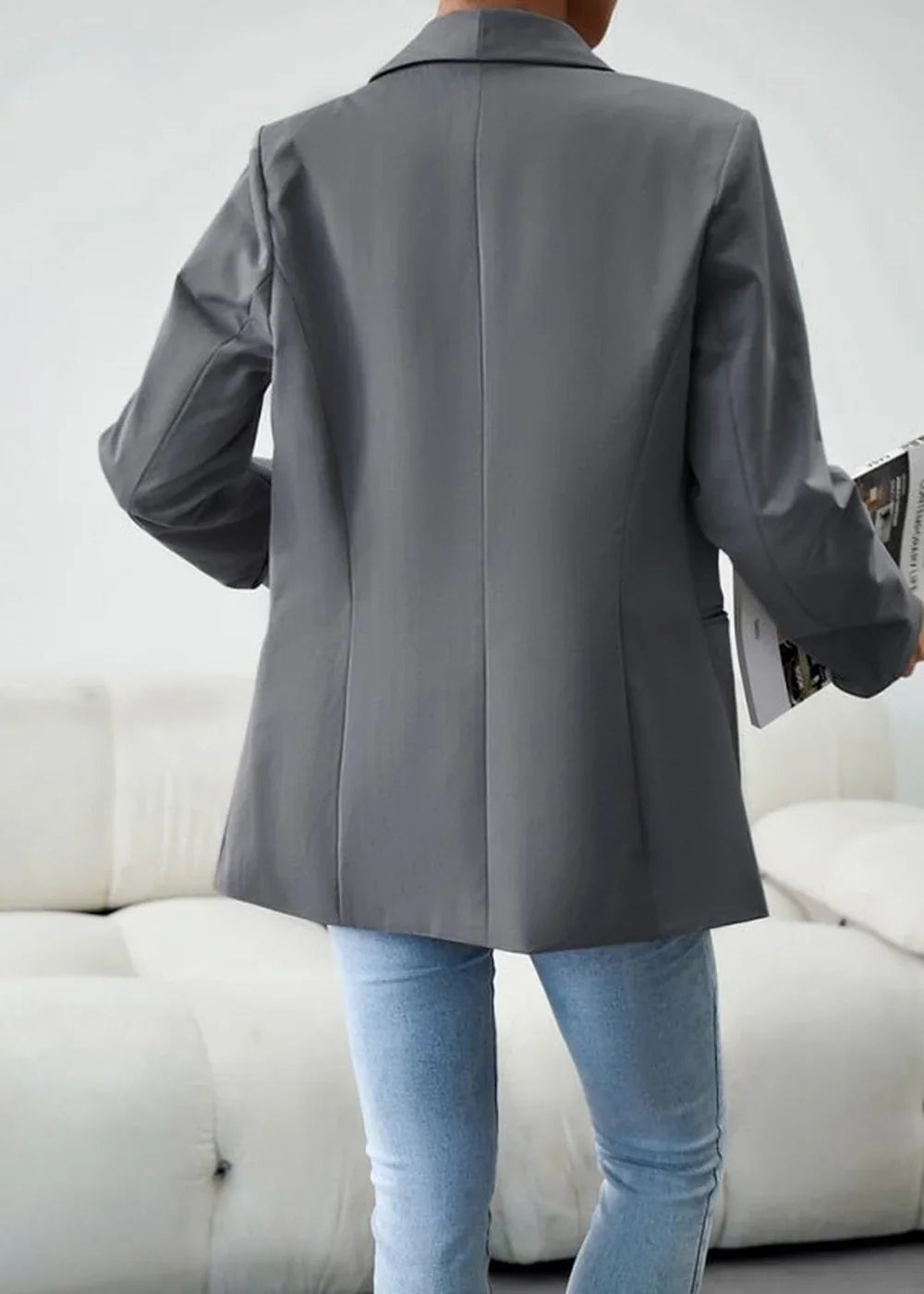 Back view of a grey polyester blazer with a smooth texture worn over light blue jeans.