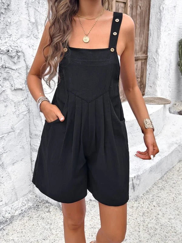 Black cotton romper with button straps and pleats, worn by a model.
