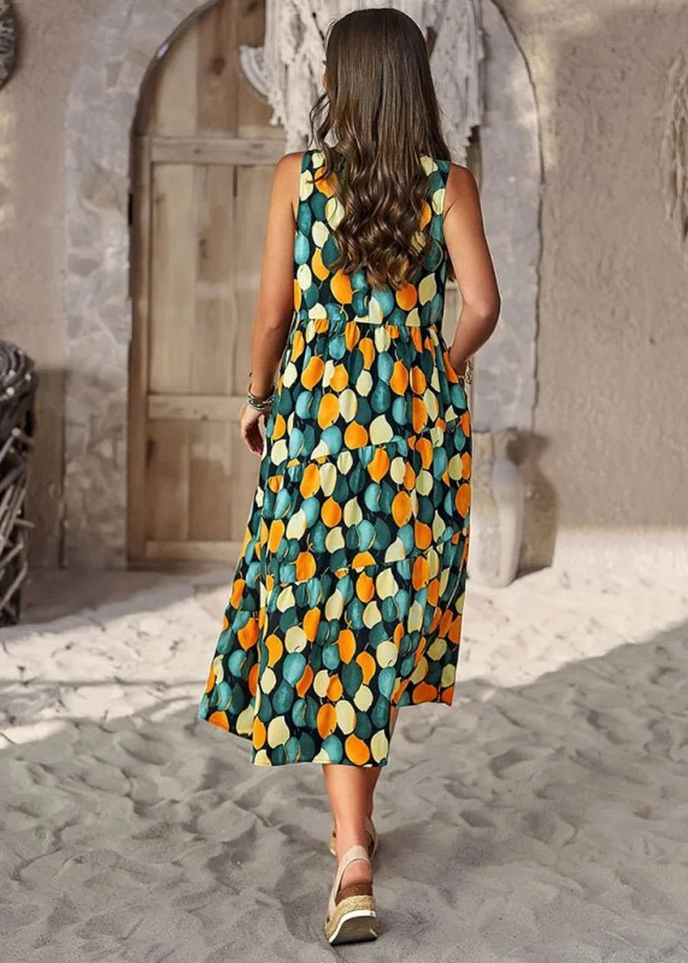 Woman in a tiered, sleeveless, dark green dress with an all-over abstract leaf print in teal, orange, and yellow.