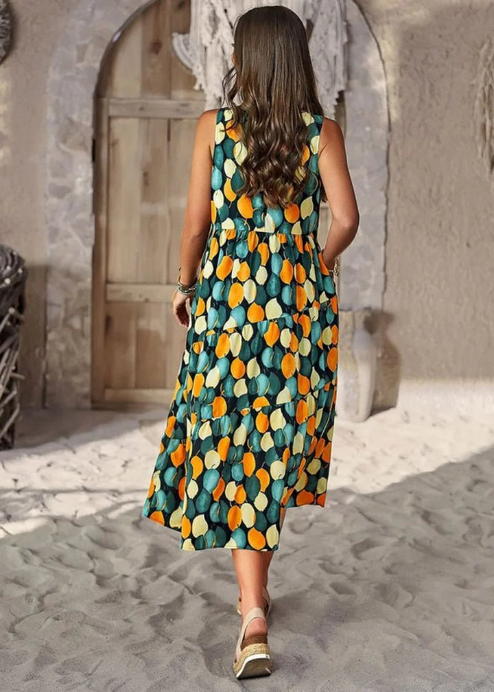 Woman in a tiered, sleeveless, dark green dress with an all-over abstract leaf print in teal, orange, and yellow.