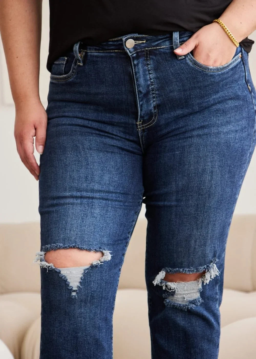 Close-up of distressed dark wash denim jeans with ripped knees and frayed edges.