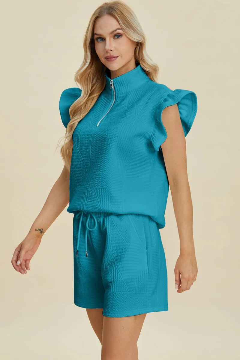 Teal textured short suit with ruffled cap sleeves and a quarter-zip neckline on a model.