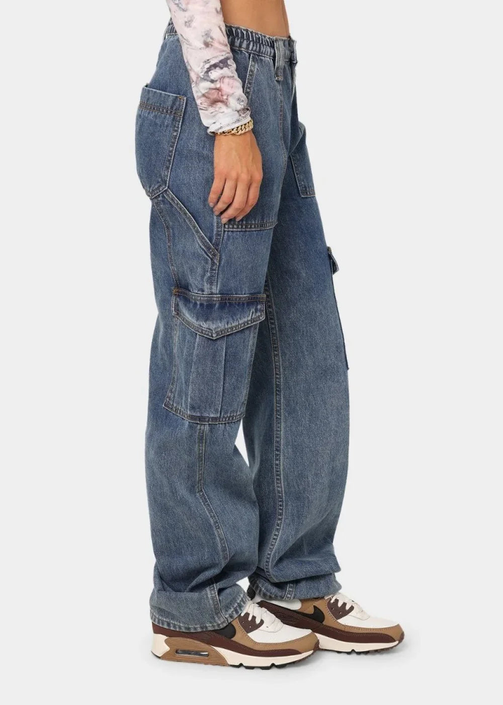 Side view of a person wearing light-wash denim cargo pants with multiple pockets and white and brown sneakers.