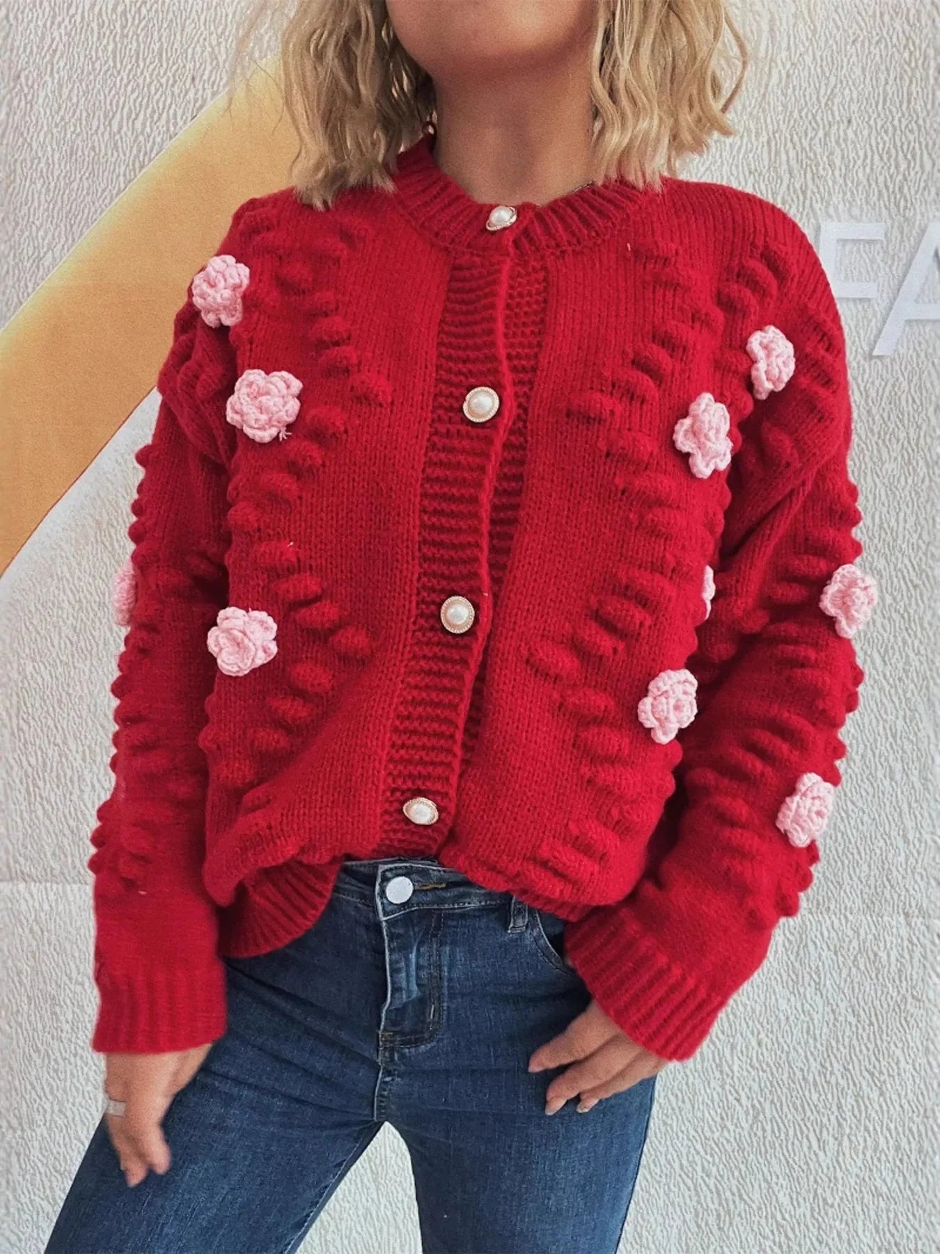 Red knit cardigan with pink floral appliques and pearl buttons, paired with dark wash jeans.