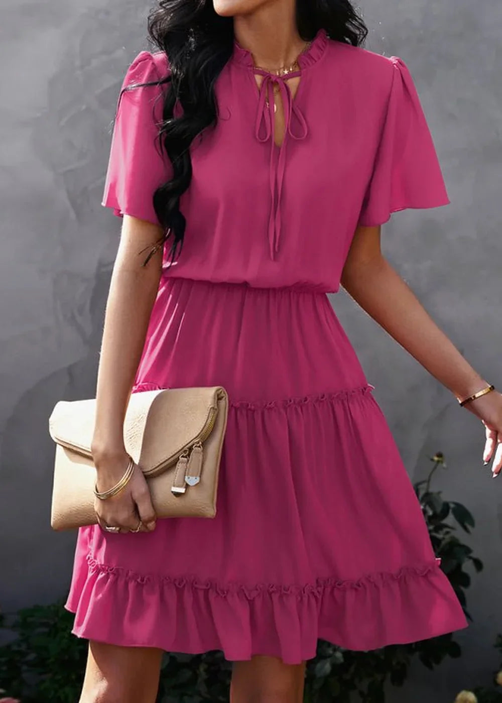 Fuchsia ruffled tiered dress with tie-neck detail and neutral clutch.