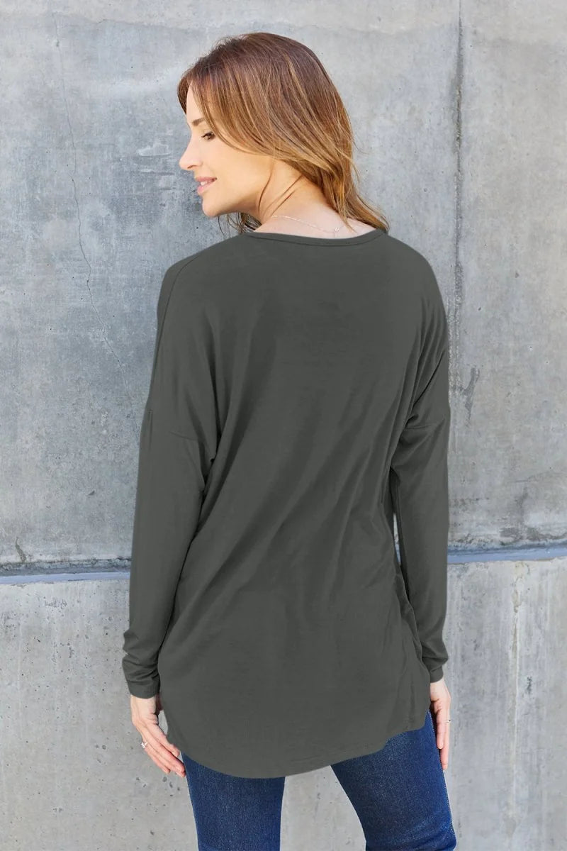 Back view of a woman wearing a dark gray, long-sleeved, relaxed-fit t-shirt made of soft rayon and spandex blend.