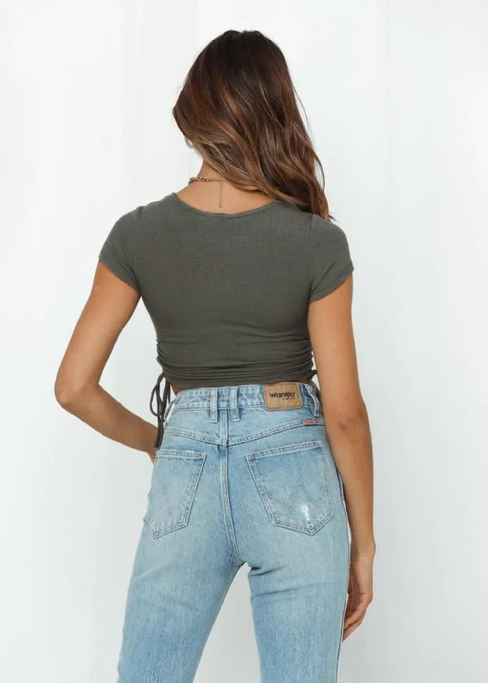 Back view of a woman wearing a dark olive green ribbed crop top with cinched sides and light wash high-waisted jeans.