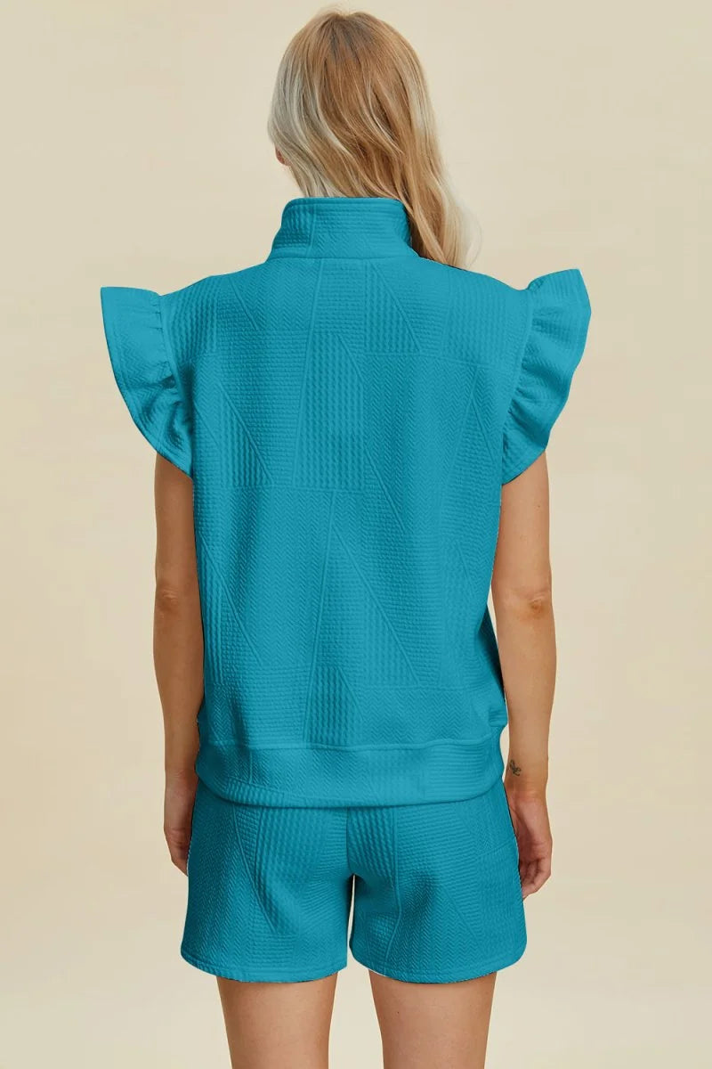 Back view of a teal quilted short suit with ruffled cap sleeves and a mock neck.