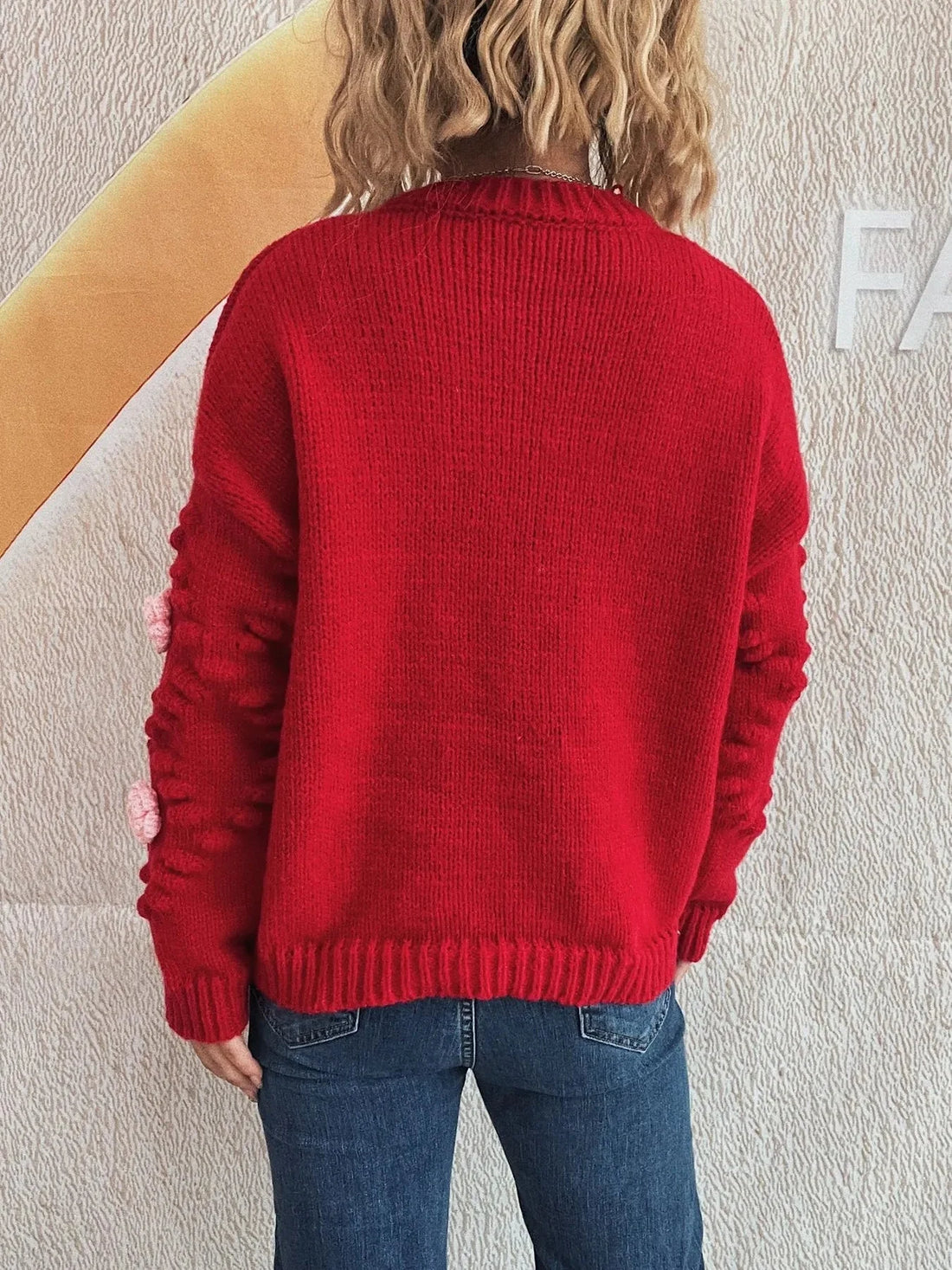 Red knit sweater with floral sleeve details and blue denim jeans.