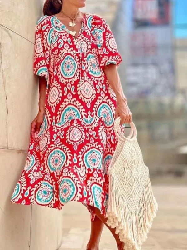Red midi dress with geometric pattern, v-neck, and a fringe macrame bag.