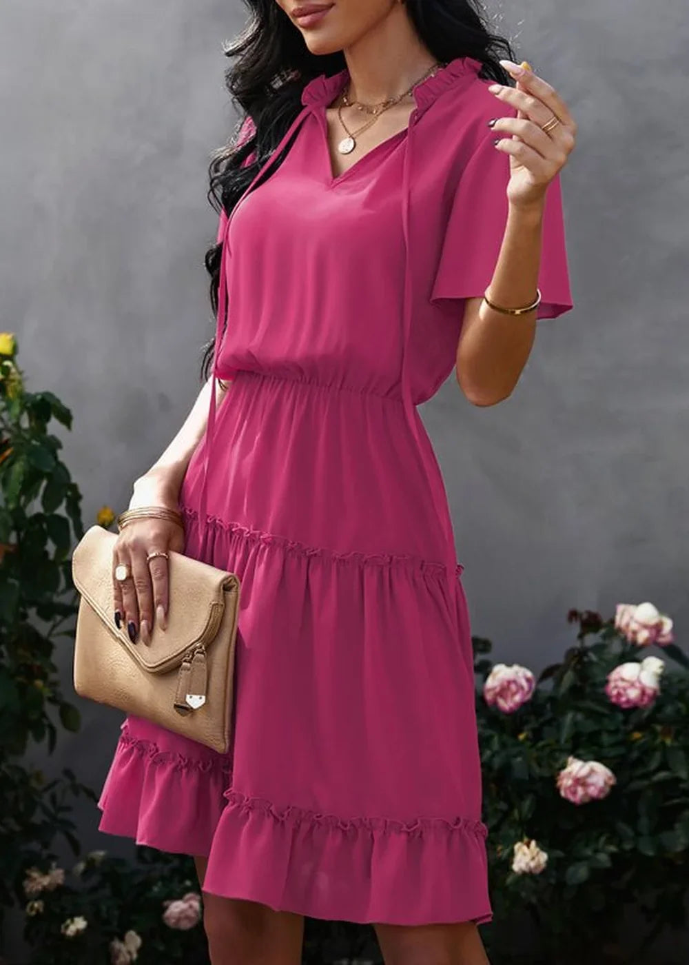 Fuchsia tiered ruffle dress with V-neck and tie, cinched waist, on model with clutch.