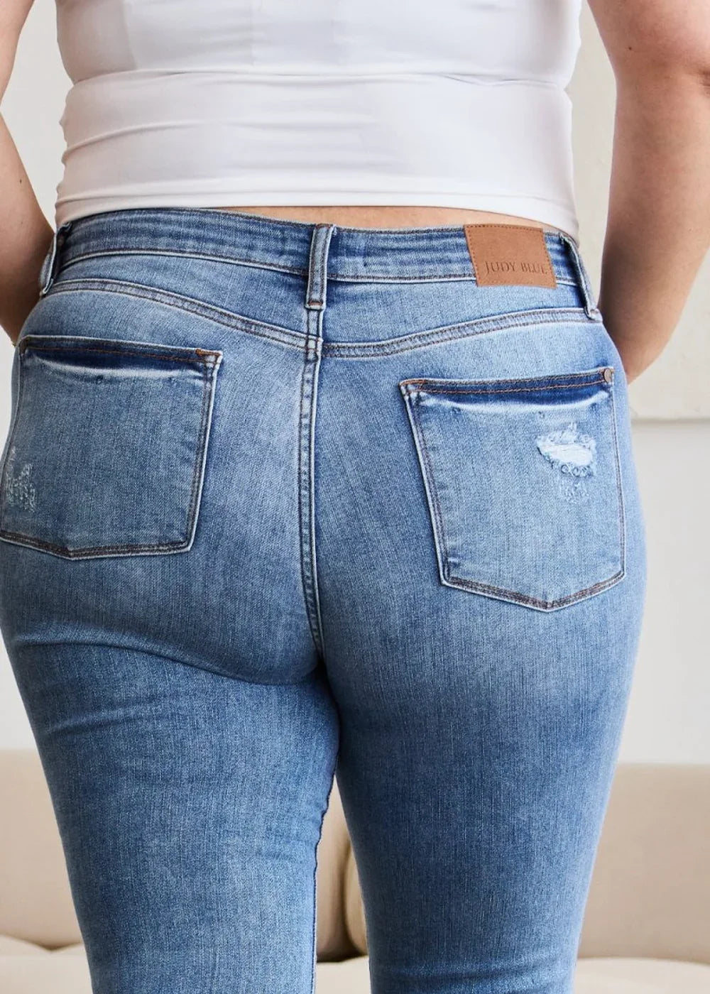 Close-up of distressed medium wash denim jeans showing back pockets and a leather patch.