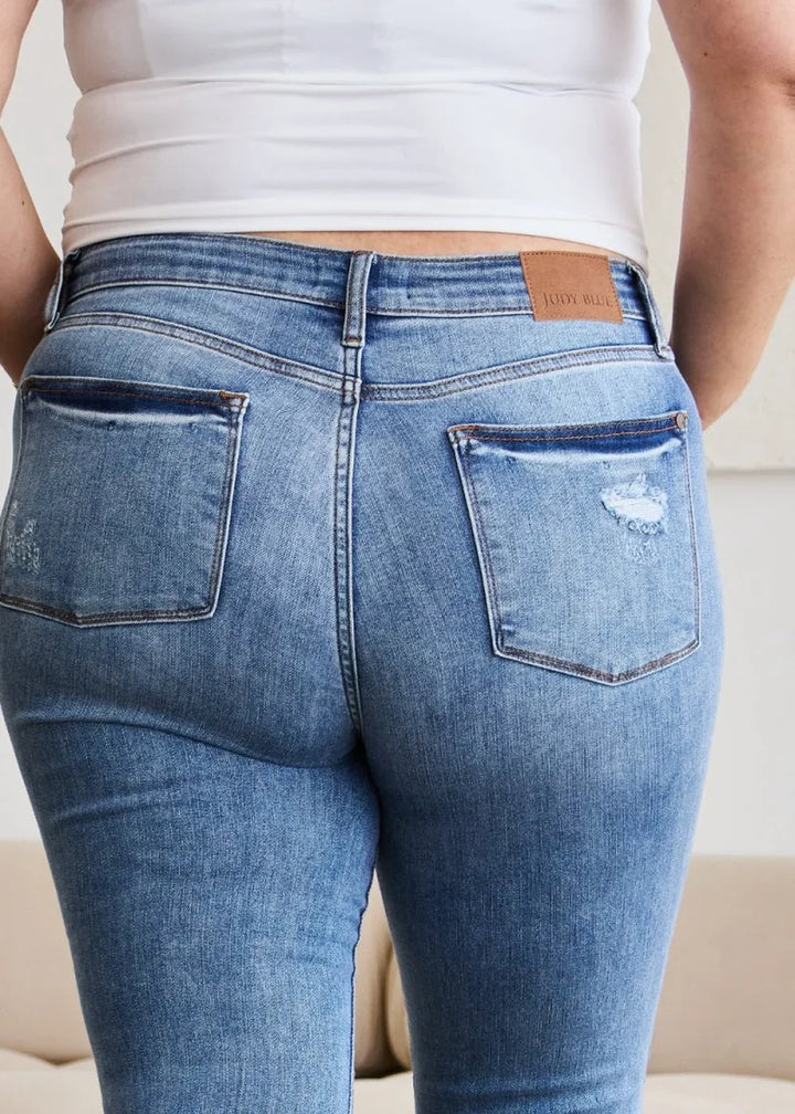 Close-up of distressed medium wash denim jeans showing back pockets and a leather patch.