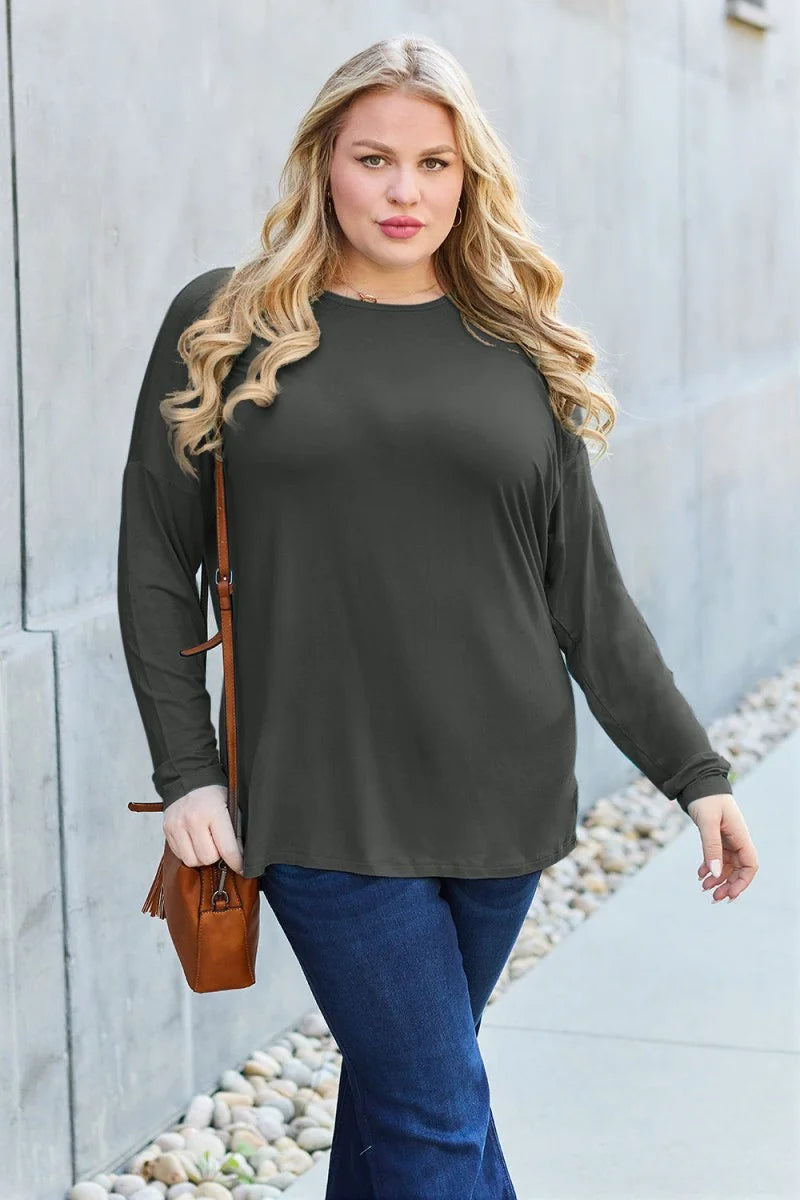 Woman in a dark olive long-sleeve top and dark wash jeans, with a brown crossbody bag.