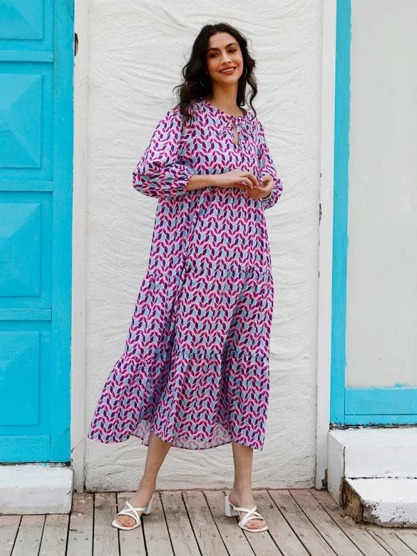 A woman in a tiered, geometric print midi dress with a tie-neck and white block heels.