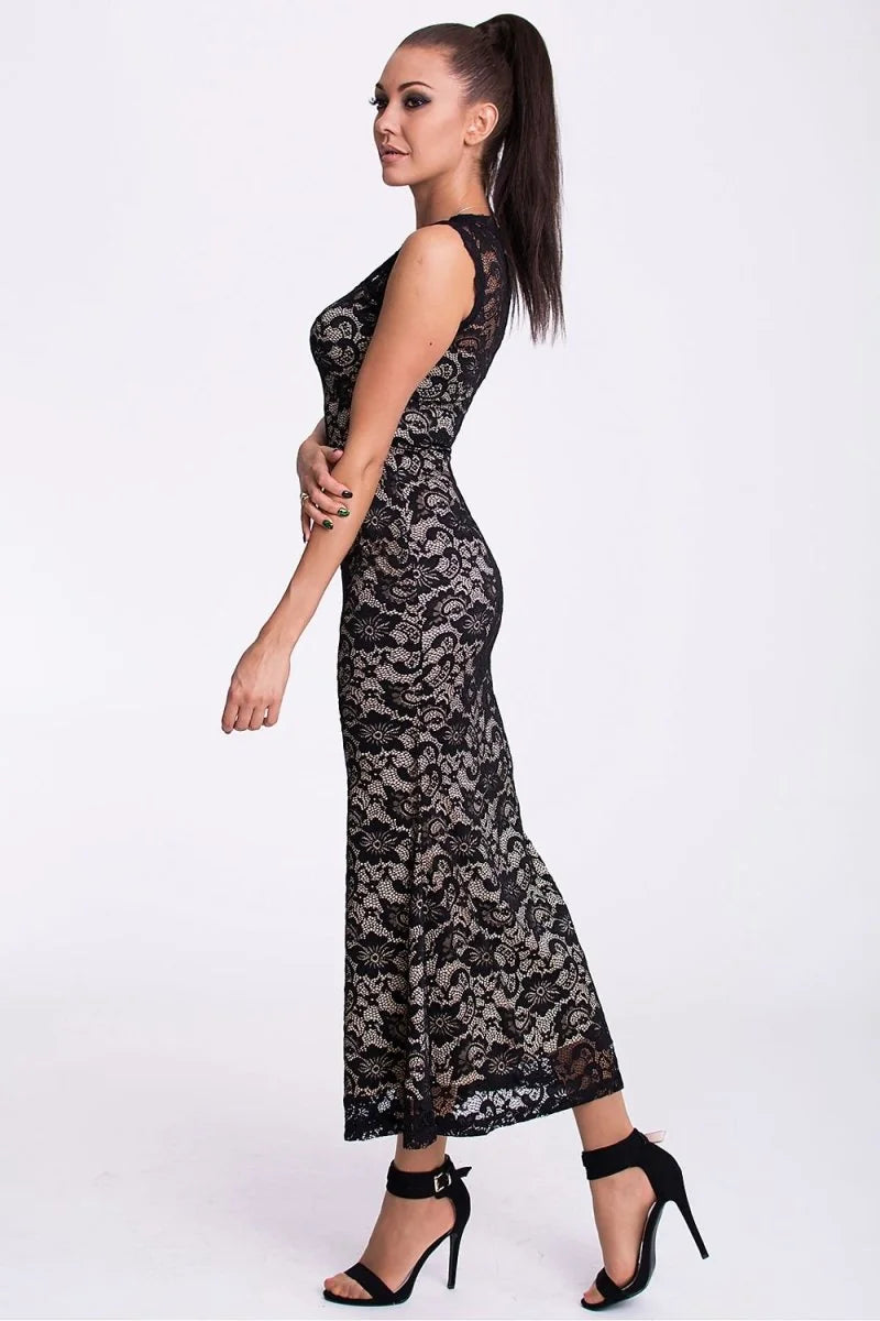 Woman in a fitted black lace maxi dress with nude lining and black ankle-strap heels.
