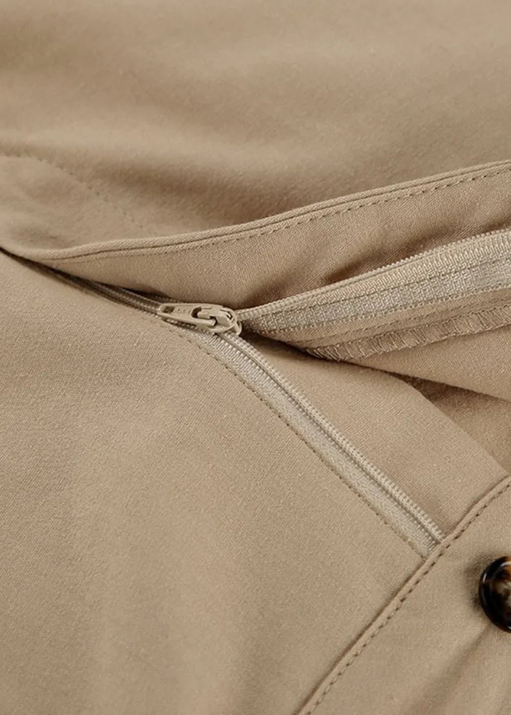 Close-up of a beige short suit showing a zipper detail and a button.