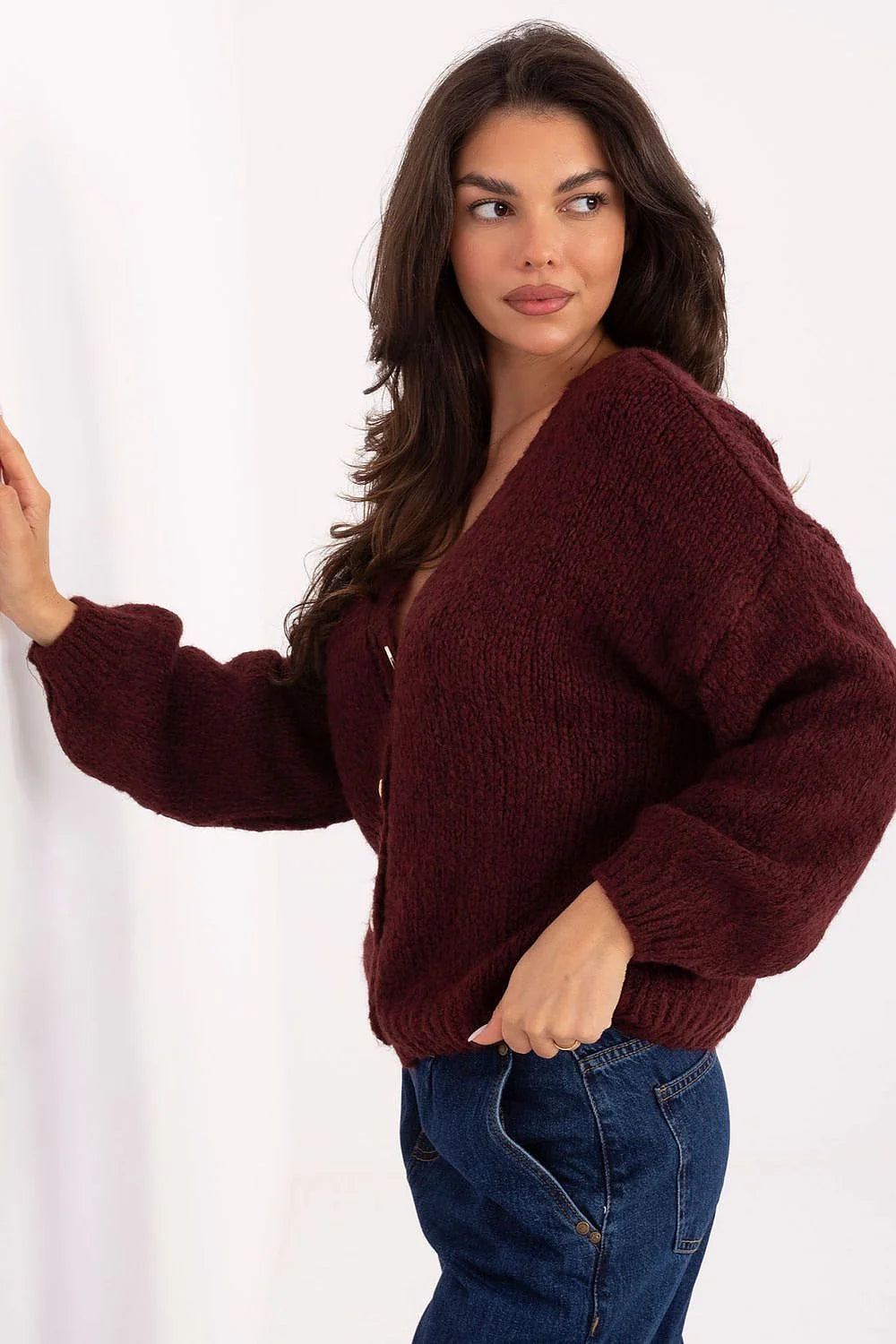 Woman in a maroon knit cardigan with balloon sleeves and dark wash jeans.