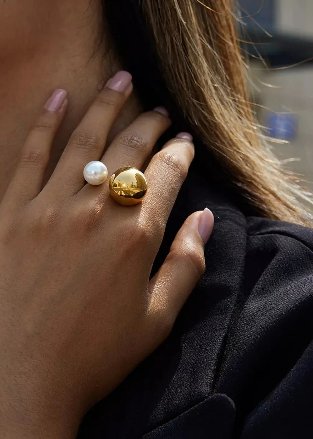 Close-up of a hand wearing a gold-plated ring with a large gold sphere and a white pearl.