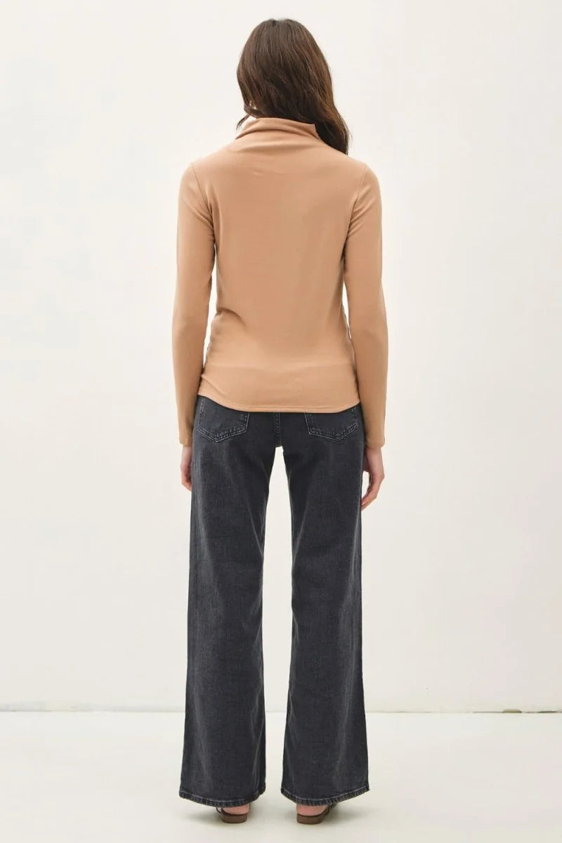Back view of a woman wearing a camel turtleneck top and dark wash wide-leg jeans.