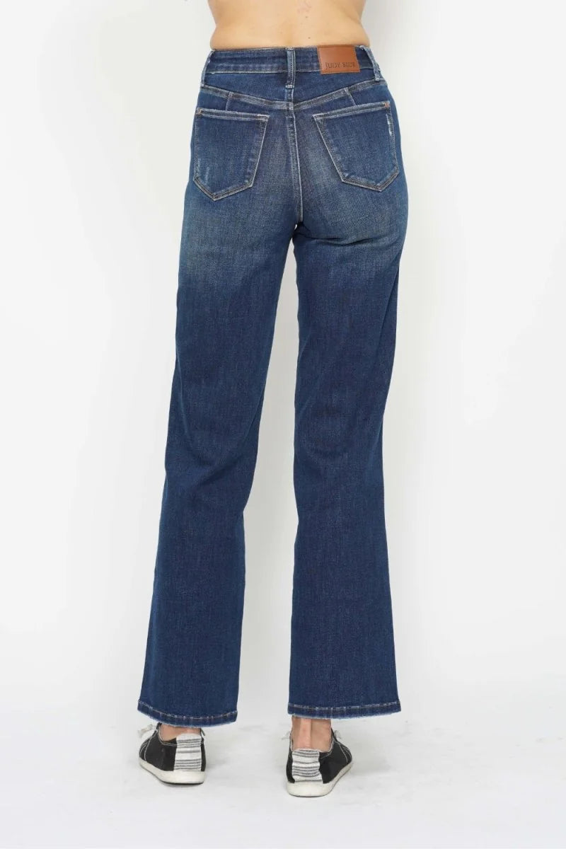 Back view of dark wash, distressed denim jeans with a straight leg style and a brown leather brand patch.