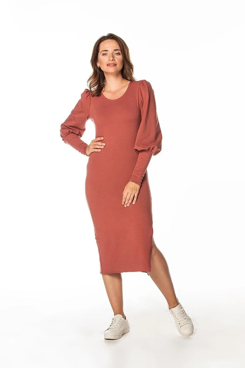 A woman in a rust-colored long-sleeved midi dress with puffed sleeves and white sneakers.