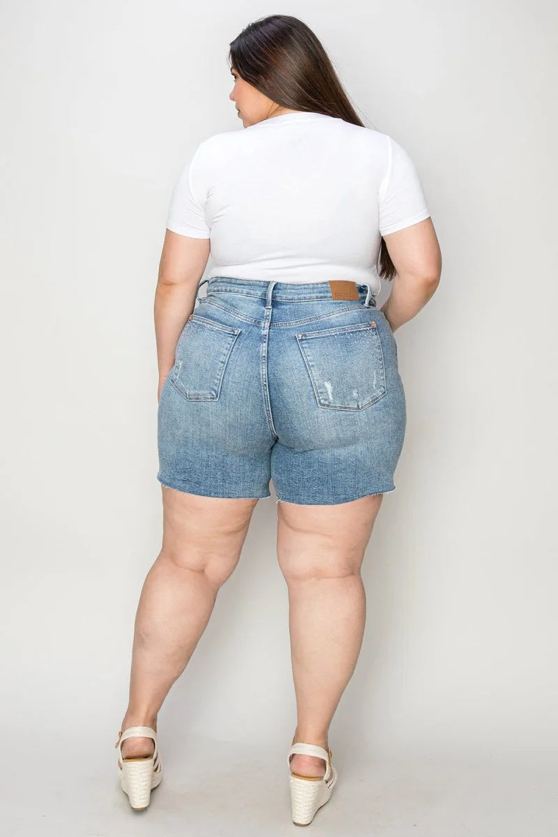 Back view of light wash distressed denim shorts with a high waist and frayed hem on a model.