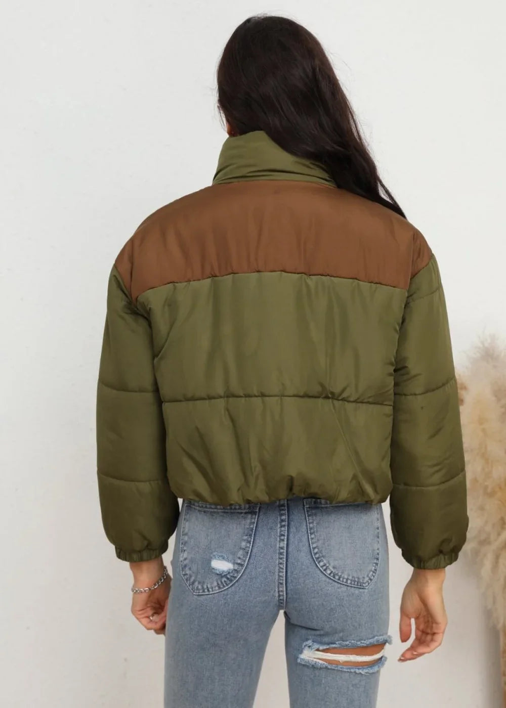 Back view of a cropped puffer jacket in olive green with a brown yoke and collar, paired with distressed light wash jeans.