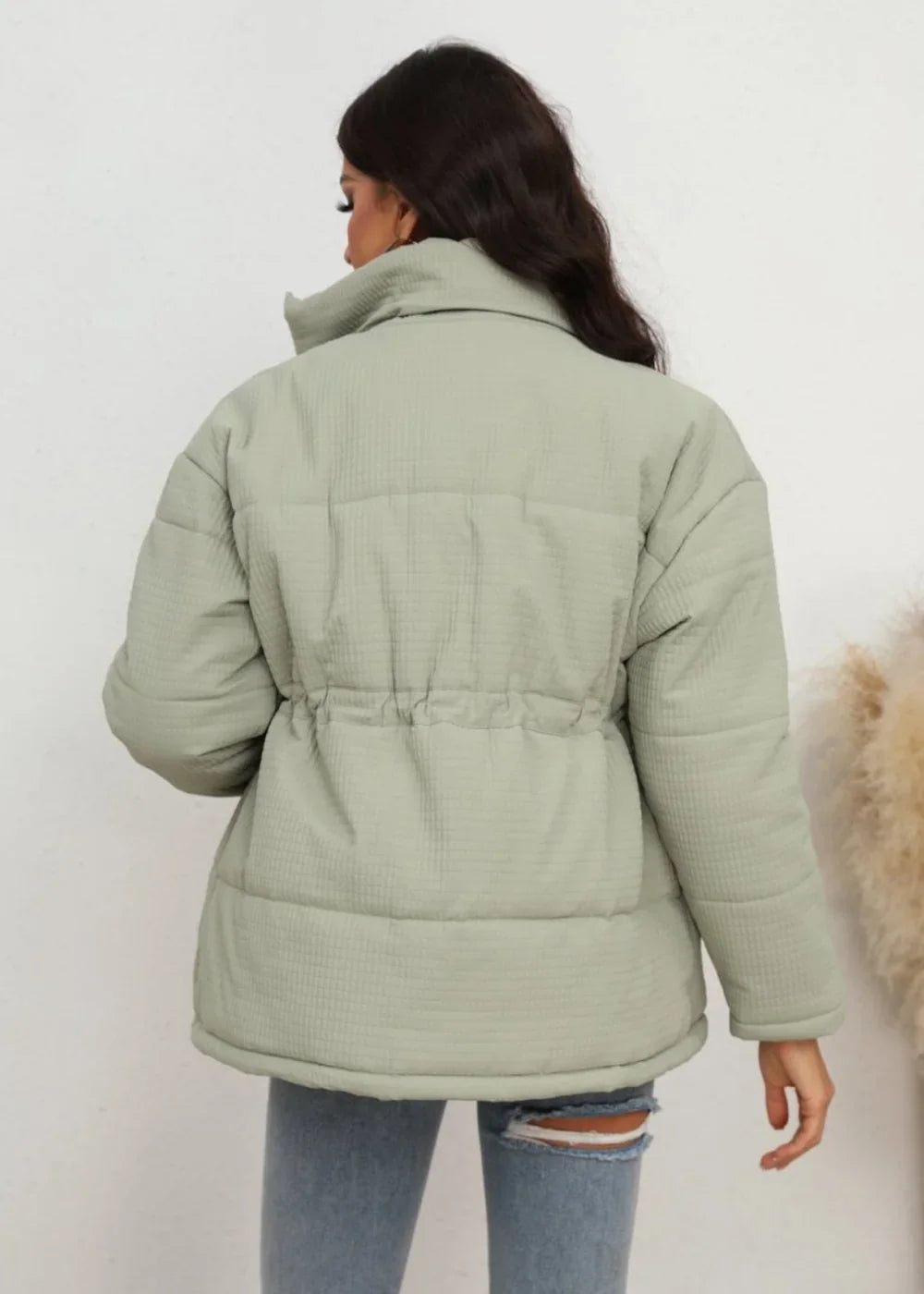Back view of a light green quilted puffer jacket with a cinched drawstring waist and high collar.