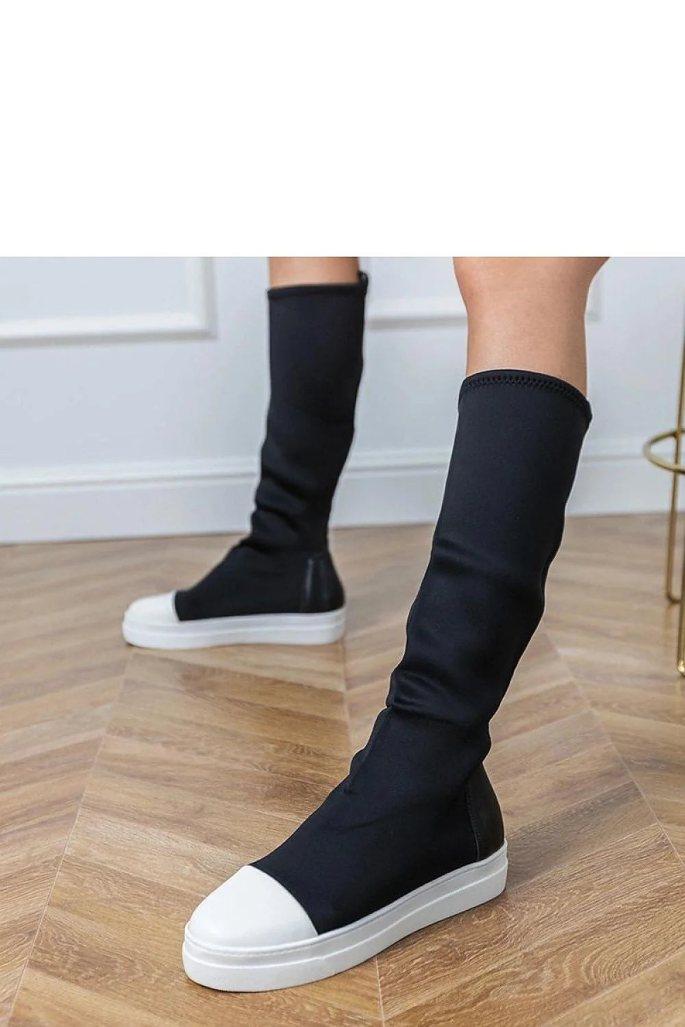 Black knee-high boots with white toe caps and white soles, worn on a model.