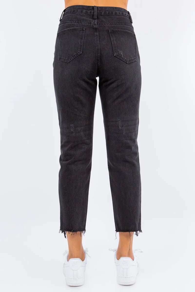 Back view of high-waisted black distressed denim jeans with frayed hem and white sneakers.