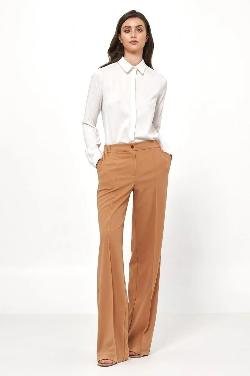 Full-length shot of a woman wearing a white collared shirt and tan wide-leg pants.