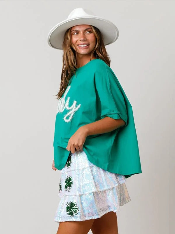 Green t-shirt with white "baby" graphic and sequined tiered shamrock skirt on model.