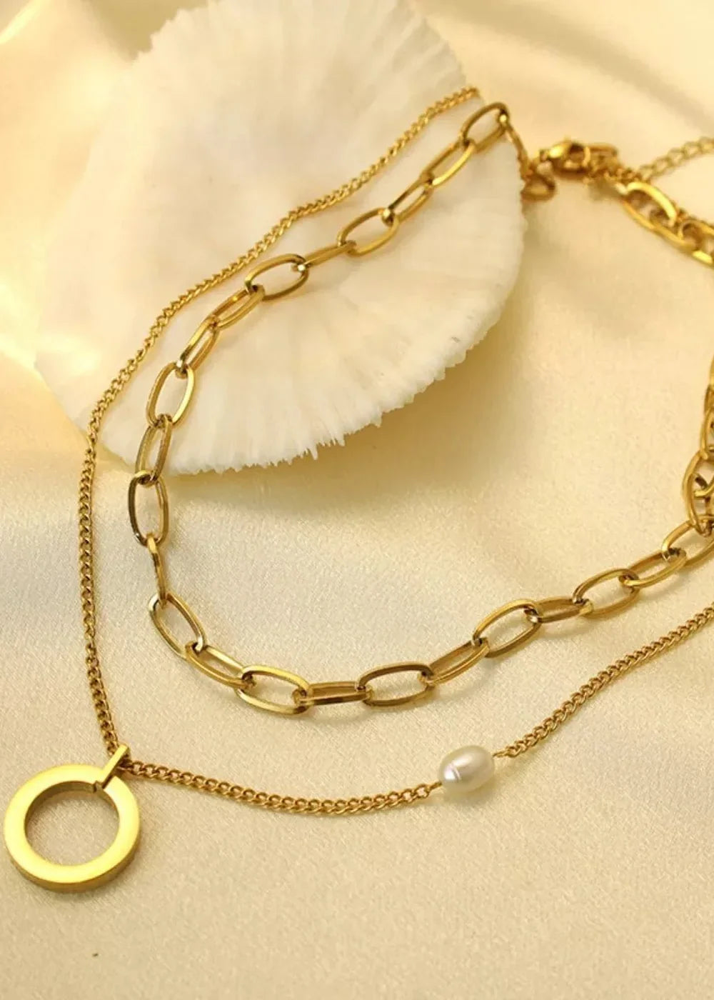 Layered gold necklace with oval links, a circular pendant, and a single pearl.