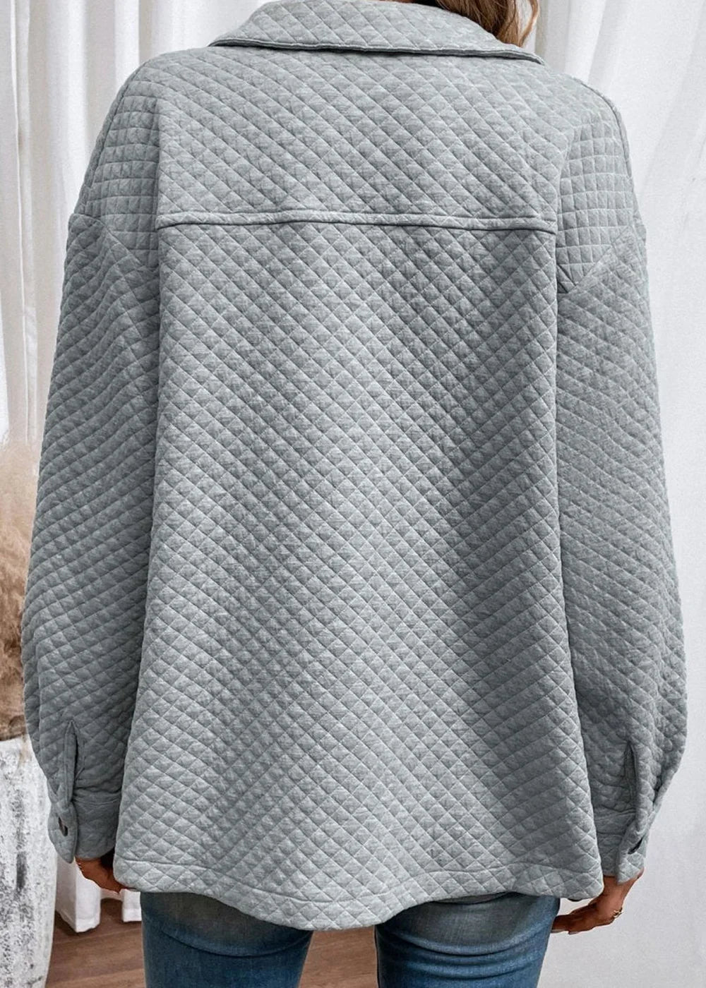 Back view of a light grey quilted jacket with diamond pattern and a pointed collar.