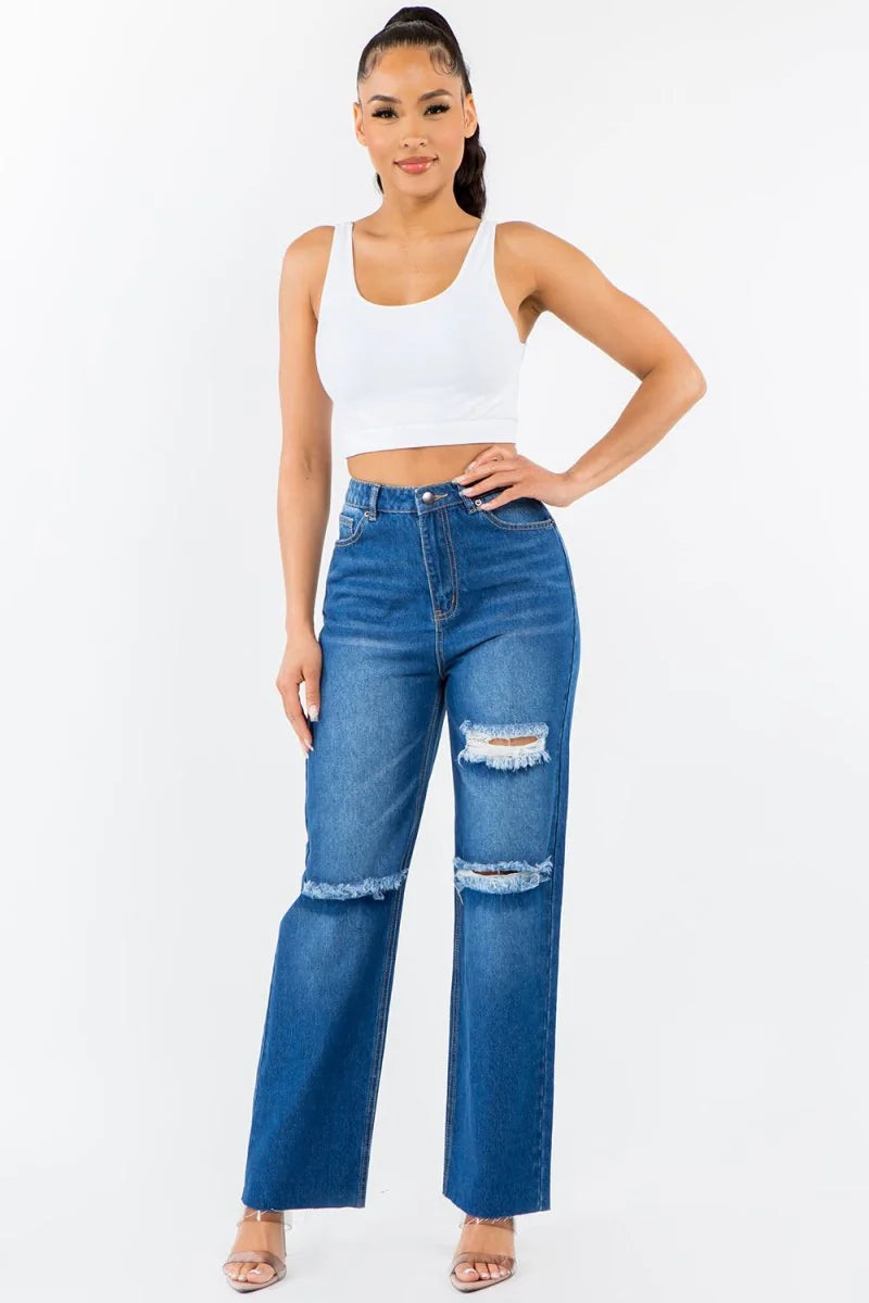 Blue distressed denim jeans with frayed hems and rips, on model.