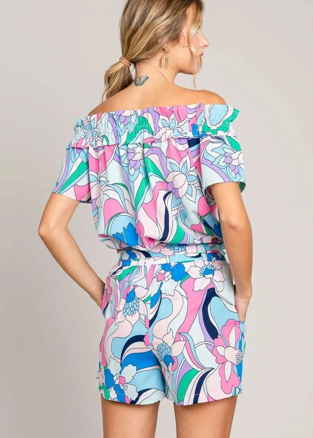 Off-the-shoulder romper with a vibrant floral print in pink, blue, and green, featuring ruffled trim.