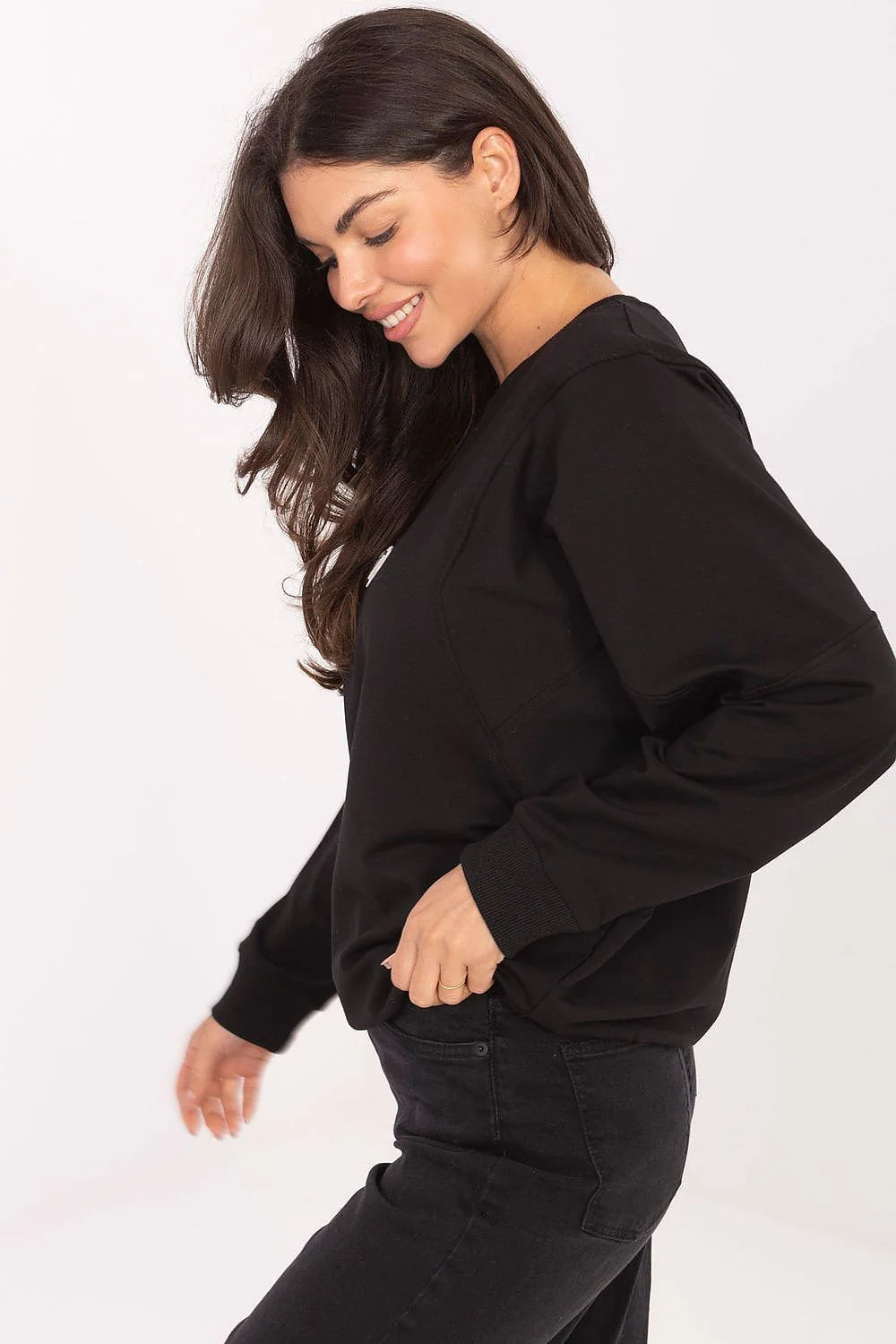 Black long-sleeved sweatshirt on a model, with a ribbed cuff and dark wash jeans.