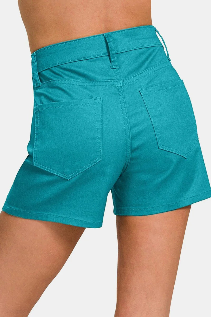 Close-up of teal denim shorts with a regular fit, showing back pockets and belt loops.