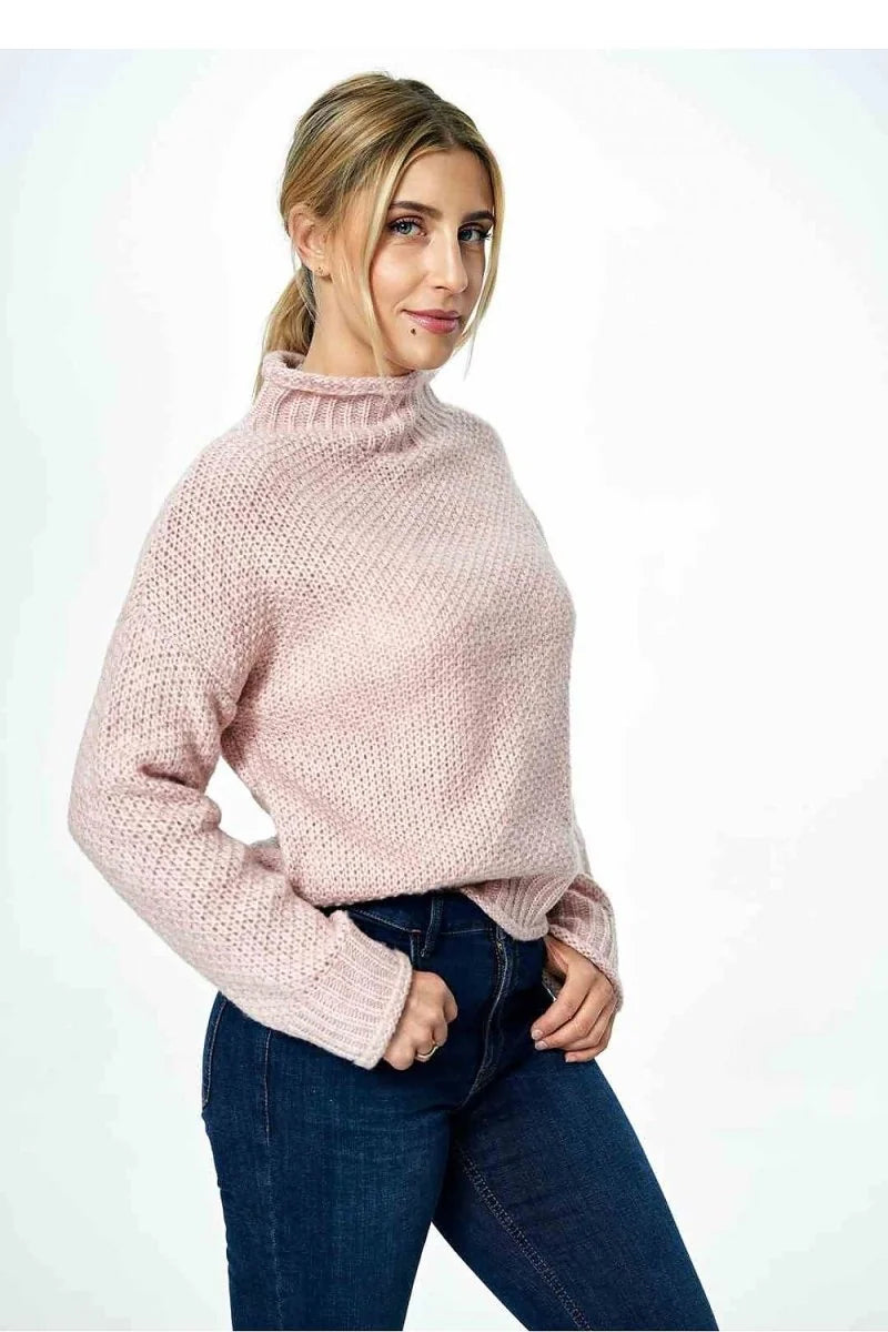 Pink knitted turtleneck sweater with textured pattern on model.