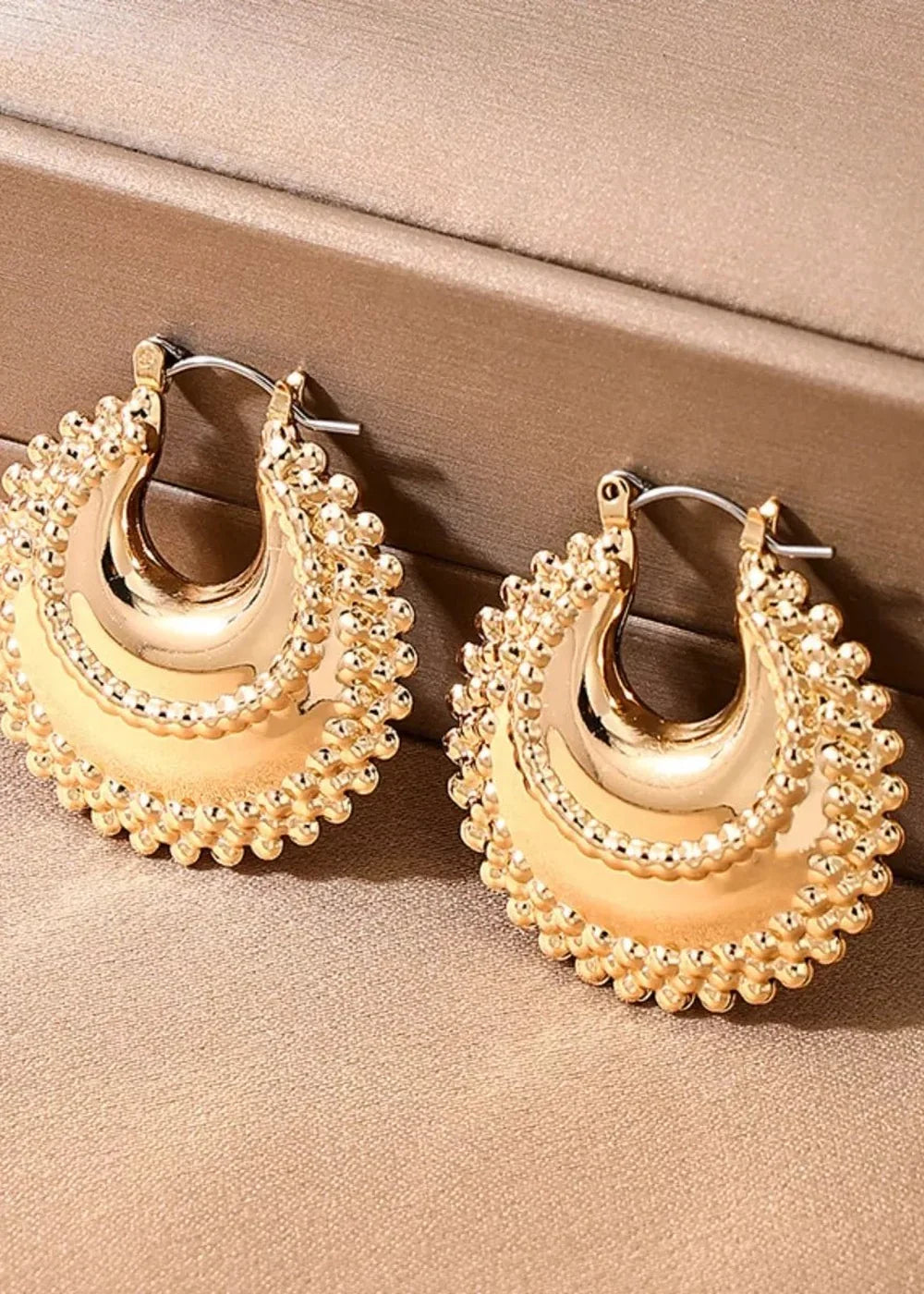 Close-up of gold-toned hoop earrings with textured beaded edges and a polished concave center.