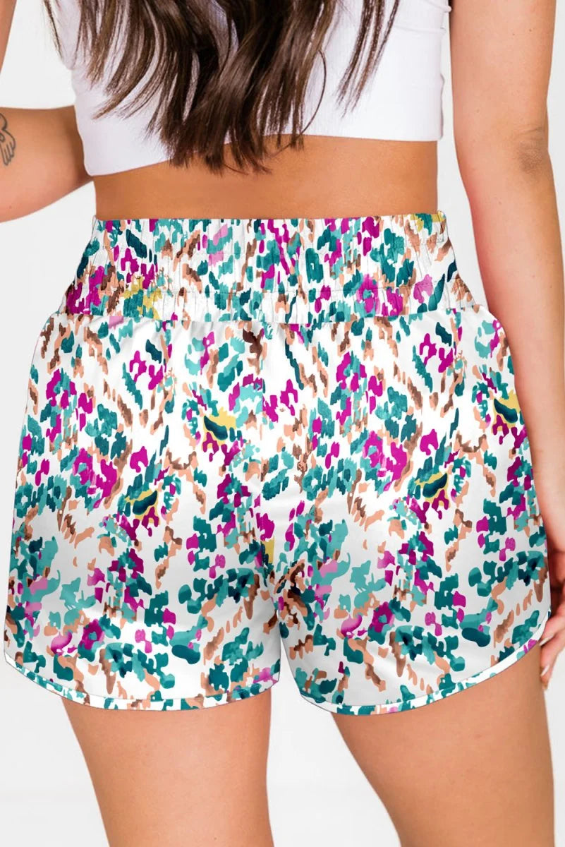 White shorts with a colorful abstract print in pink, teal, and brown, featuring a regular fit and elastic waist.