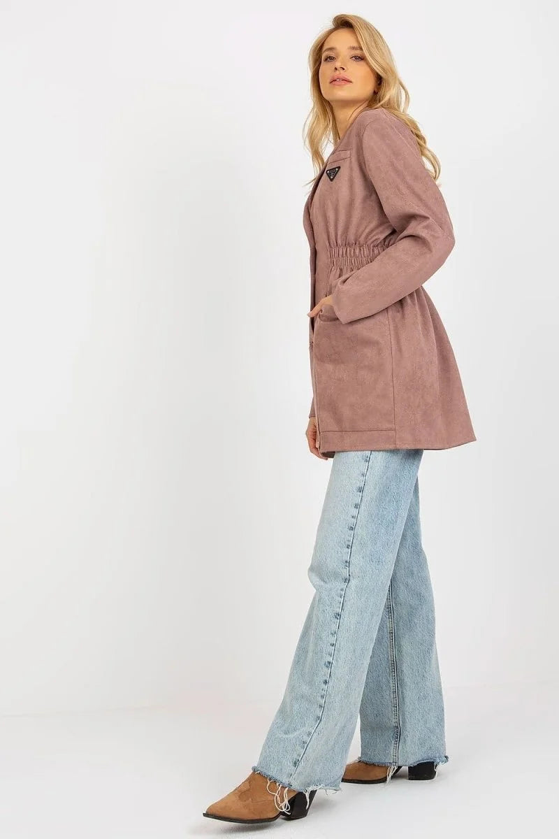 Woman in dusty rose jacket with cinched waist and light wash jeans with frayed hem, side view.